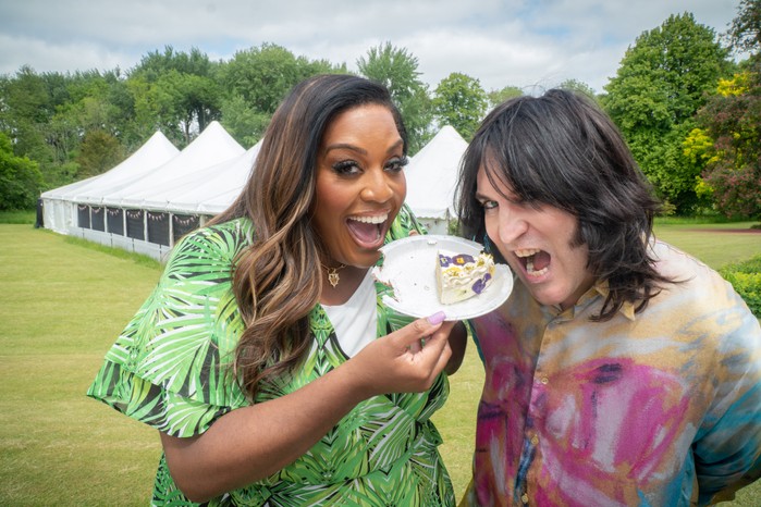 Noel Fielding and Alison Hammond standing together, pretending to eat a slice of cake