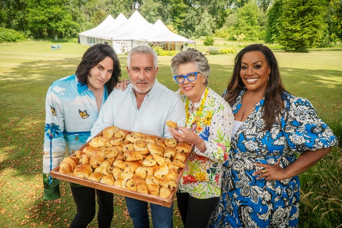 Noel, Paul, Prue & Alison on The Great British Bake Off 2023 holding a large tray of pastries, looking into camera