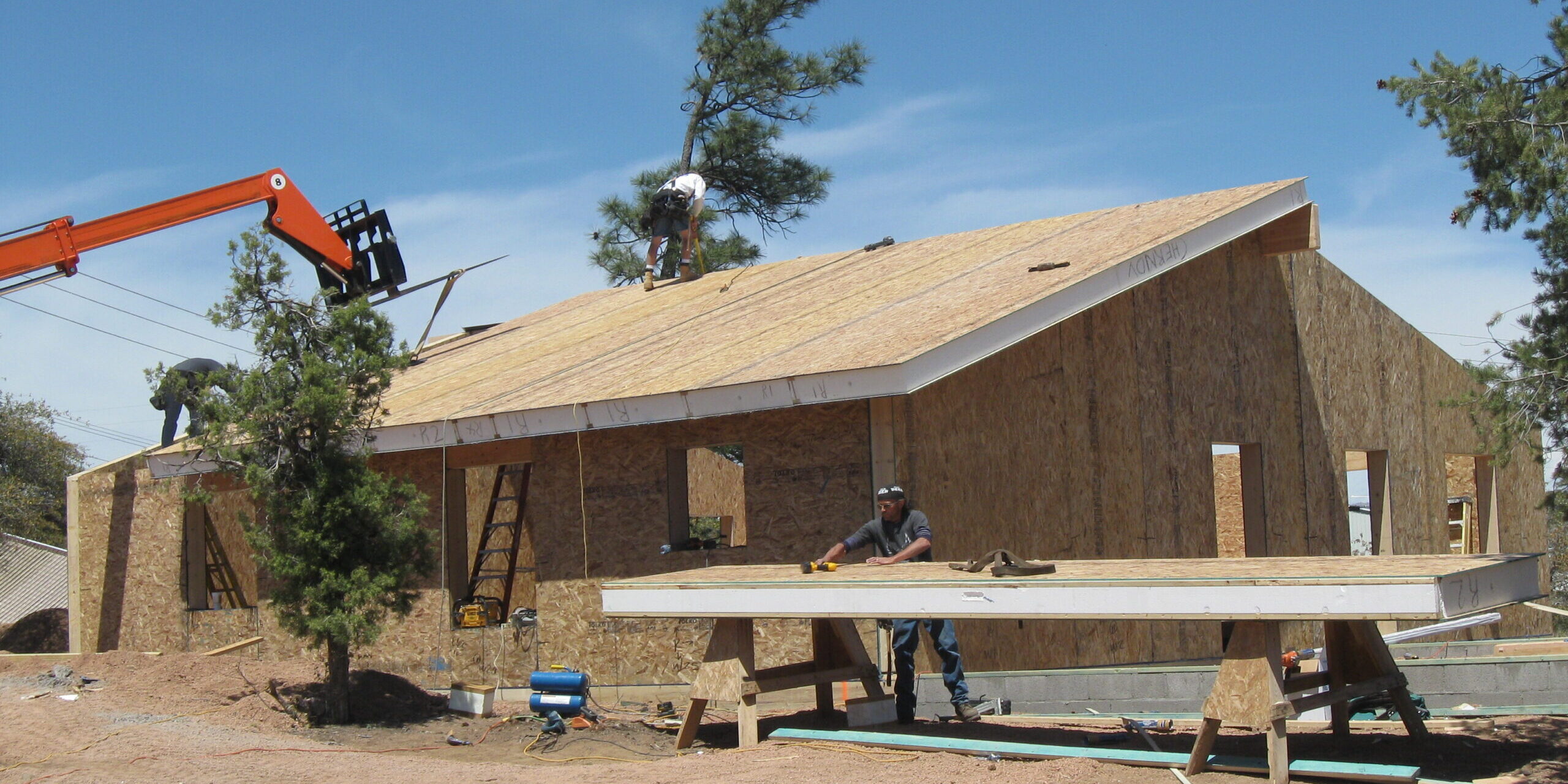 exterior of SIP home under construction; crane and workmen place roof panels – photo