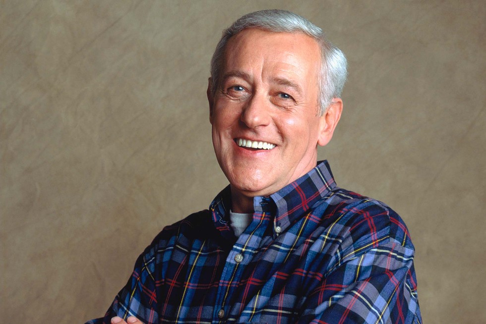 John Mahoney stands with his arms crossed, smiling for the camera