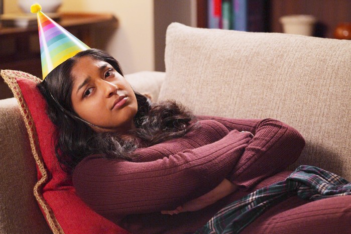 A sad Devi lying on a sofa wearing a party hat
