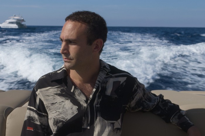 Khalid Abdalla as Dodi Fayed in The Crown season 6 sat aboard a yacht staring to the left of the frame.