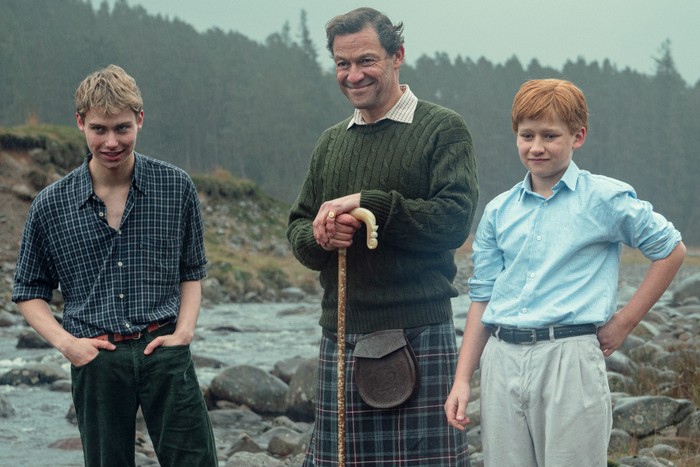 Prince William played by Rufus Kampa and Prince Harry played by Fflyn Edwards on the right with Charles, Prince of Wales played by Dominic West, standing between them leaning on a walking stick in The Crown season 6.